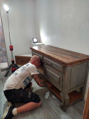 Scott Lunetta works on melding the new vanity with the plumbing for the sink.