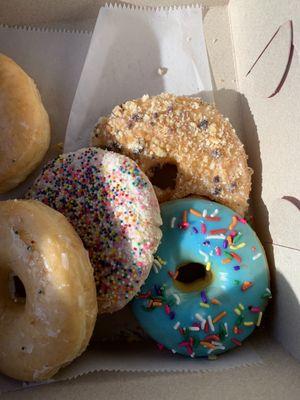 Some regular and blue sprinkle glazed donuts, a sprinkle cookie, the blueberry crumble donut.