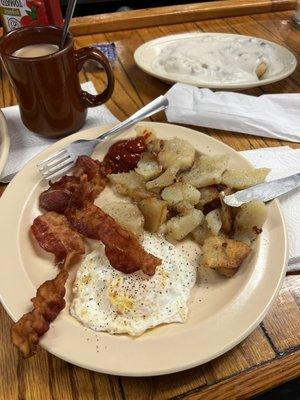 Bacon egg and fried potatoes, with biscuits and gravy in the back.