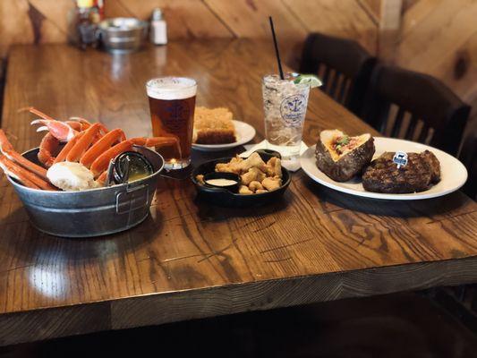 A meal for two: crab legs, gator bites, and a tender steak with a baked potato