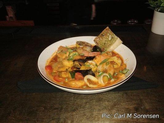 Cioppino, consisting of saffron tomato broth, shrimp, calamari, muscles, salmon, and sea bass.