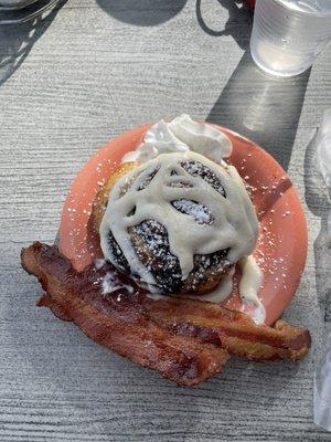 Cinnamon roll with cream cheese frosting and a side of bacon