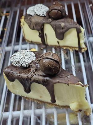 Close-up of a slice of one of the cheesecakes with chocolate toppings and a chocolate truffle on top.