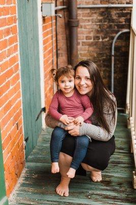 Mom and daughter smile while sitting barefoot on a New Orleans balcony.