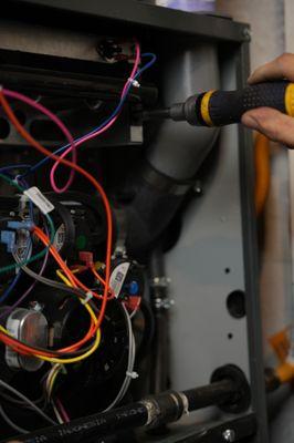 A picture of a panel open with exposed wires and a hand holding a screwdriver to repair something