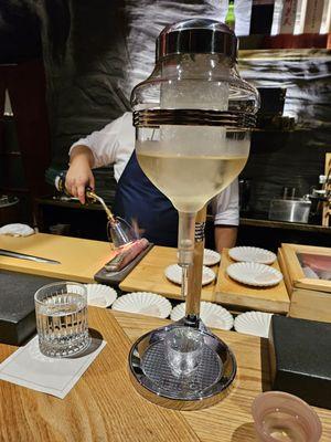 Sake dispenser. Chef torches the fish in the background.