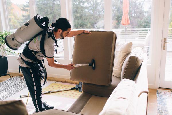 Vacuuming under couch cushions as part of our routine home cleaning service.