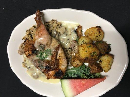 Cornish game hen on top of long grain and wild rice with sausage dressing served with roasted potatoes and a chicken suprém sauce