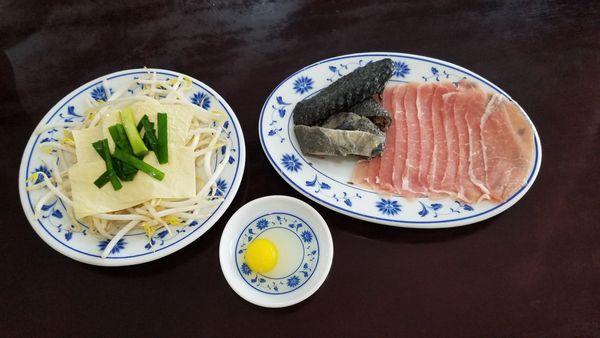 Ingredients for the dish - dried tofu skins, bean sprouts, black chicken, slices of pork, a quail egg, and green onions.