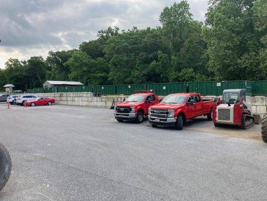 A fleet of red trucks and dumpsters lined up, showcasing Eagle Transfer Services' equipment for efficient waste removal.