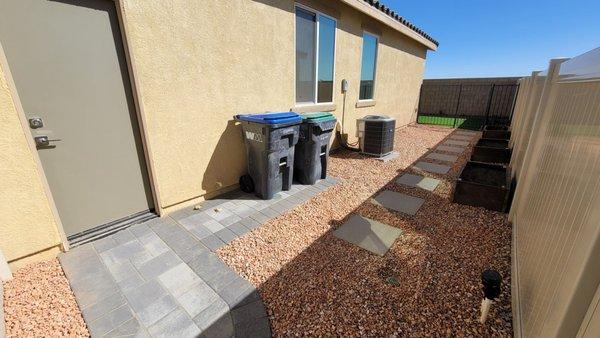 Side yard with pavers for trashcan. Stepping stones and gravel with wooden planter boxes. Iron gate leads to back of house.