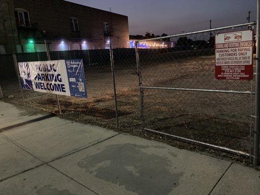 Tiny "Towing and Booting enforced" sign next to giant "Public Parking Welcome" sign.