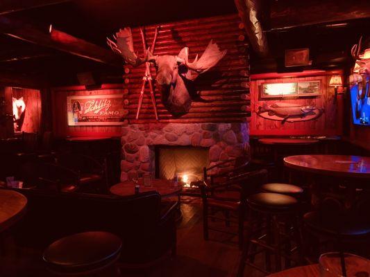 Right side of the bar area after walking in the front door, with the fireplace the main highlight. TVs along the wall to the right as well.