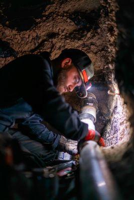 Working in a tunnel beneath the home foundation to repair a broken sewer pipe