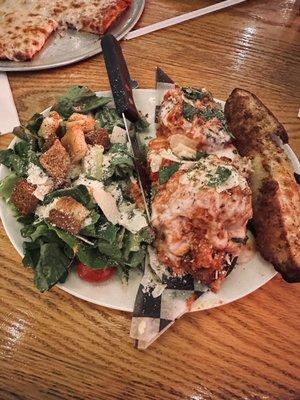 Meatball sandwich with a Caesar side salad and cheese pizza in the background