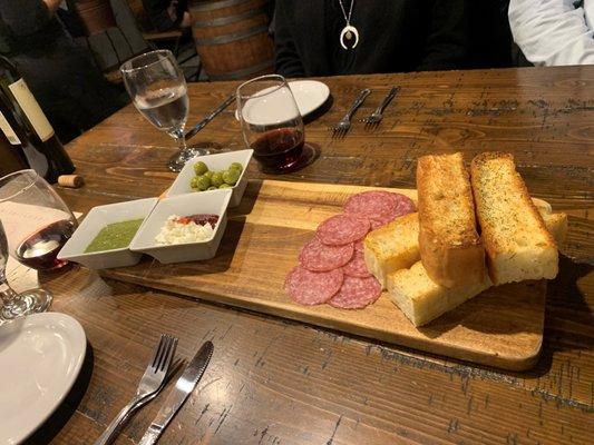 Charcuterie board with focaccia bread, salami, goat cheese with jam, olives and pesto sauce