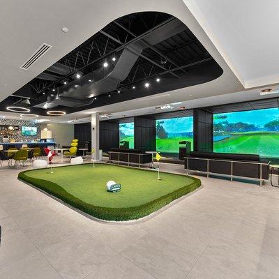 Our lobby area with a practice green, rest area and bar surrounded by driving range bays and course play bays.