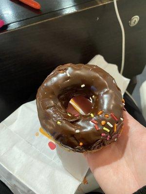 A chocolate frosted donut with barely any sprinkles