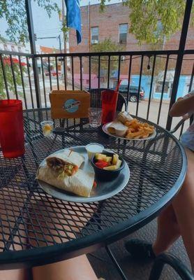 cheesesteak wrap with fruit cup, and shrimp wrap with french fries; seated at a table in the patio dining