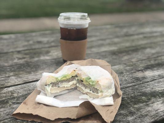 Bialy bagel with garlic cream cheese, capers, avocado, and sausage and a cold brew