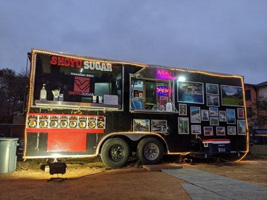 Food truck located in the back. There is parking right in front of the truck and a small eating area