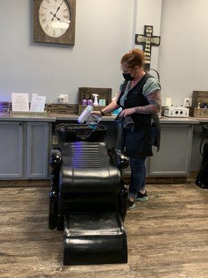 Kellie sanitizing the shampoo bowl and chair with disinfectant and blue light.