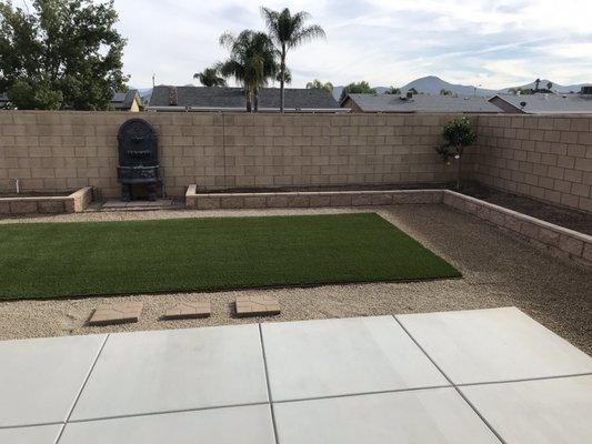 Backyard with perimeter concrete block flower bed, fountain and artificial turf