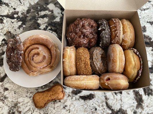 Cinnamon roll, apple fritters, dog treat and a dozen various donuts