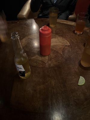 Dining table with beer and a bottle that might be ketchup