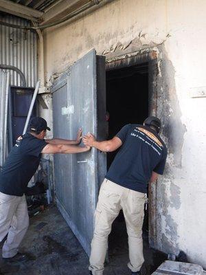 Technicians removing a walk-in cooler door during a fire damage restoration project