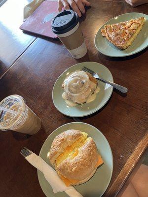 Egg and cheese bagel sandwich, cinnamon roll, sausage and red pepper quiche, banana cream iced latte, americano