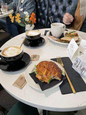 Two cappuccinos, salmon croissant sandwich, and soup and sandwich combo.