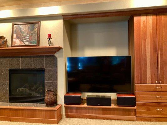 65" TV mounted on articulating arm, above 3 audiophile speakers. Components are inside the cabinet, controlled by just the cable TV remote!