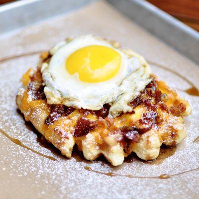 The American: liege waffle with syrup, bacon bits topped with cheese and eggs over easy. Breakfast / Brunch waffle