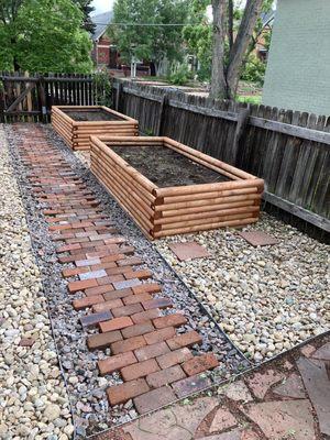 Brick walking path surrounded by quarry rock to the side gate.  Plantar boxes. River rock surrounding the boxes.