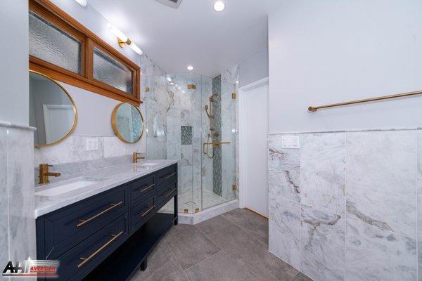 Modern bathroom in Agoura Hills by American Home Improvement. Blue vanity, white marble tile, enclosed shower and mat gold fixtures.