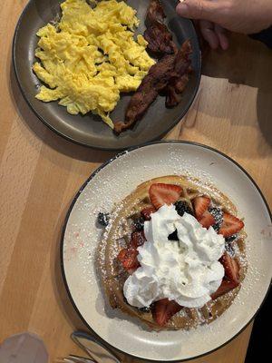 Waffle and fruit breakfast special with a side of eggs and bacon