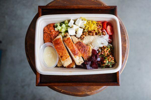 Mediterranean bowl with cous cous, beet relish, hummus, roasted red pepper purée, feta cheese, tomato, garlic toum sauce