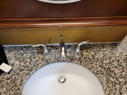 Bathroom sink, the wood frame is old and worn and there is a very poor cork job on the sink.