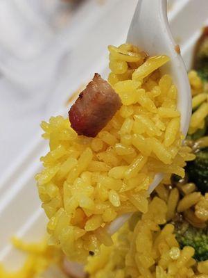 A fork holding a scoop of Pork Fried Rice with a pice of pork on top.