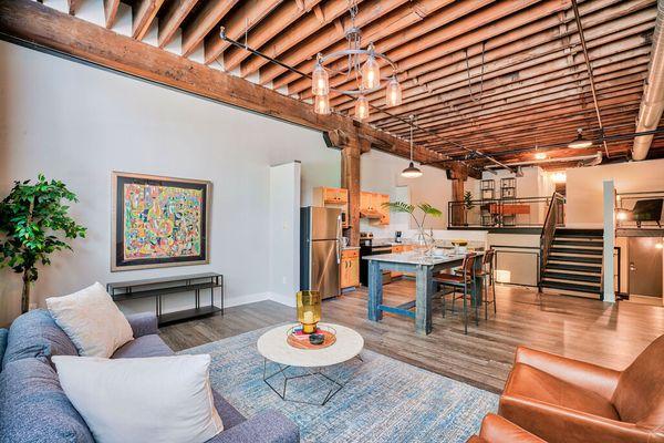 A living room with wooden ceiling panels near a kitchen with a small staircase leading to a lofted area at Wireworks Lofts in...