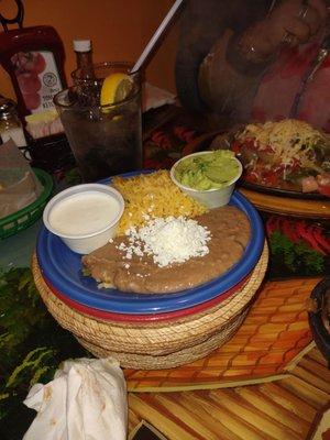 Beans and yellow rice, guac, cream and tortillas in basket.