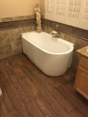 Custom corner bathtub with wood looking ceramic tile flooring