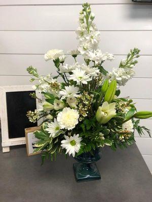 Traditional floral designed arrangement.  All whites in green glass pedestal vase.