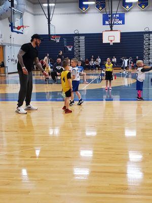 Coach is assisting 5 Year Olds play basketball on half court inside Imlay City High School Gym.  3/10/2024