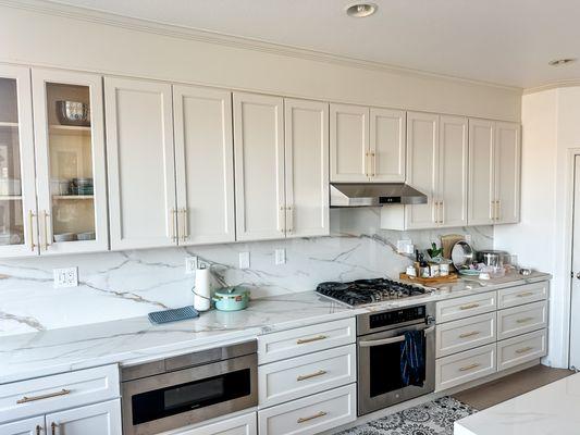 Sleek white cabinets, marble backsplash, and ample storage in this modern kitchen design with subtle yet elegant Art Deco-inspired accents.