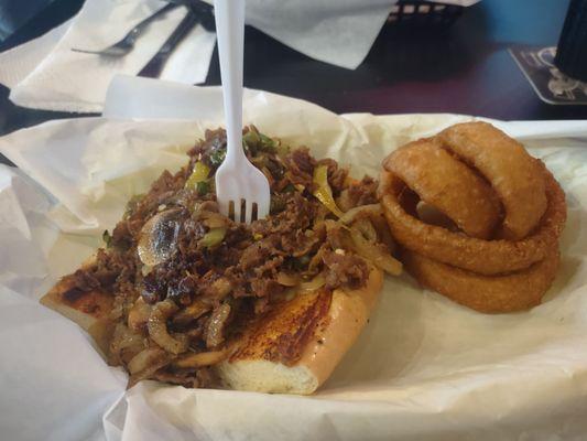 Half size Philly cheese steak with provolone cheese onions rings side.