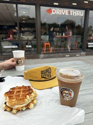 Iced latte with coffee cubes, sausage egg and cheese waffle sandwich.