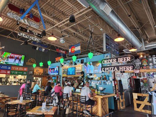 A busy bar with taps and t.v.'s. To the left is a woodburning pizza kitchen. So yummy