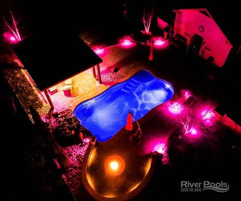 O30 inground freeform fiberglass pool with multicolored patio lights at night